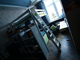 книги, альбомы и сувениры на полках открытого белого шкафа у двухэтажной кровати с лестницей, компьютерным столом у окна детской комнаты семейной квартиры