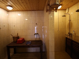 душевая комната с холодной водой в деревянной кадке под потолком и аксессуарами для бани на деревянном столе
