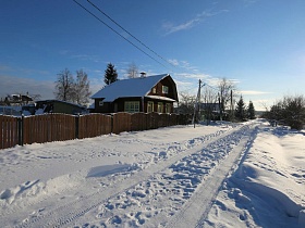 накатанная снежная дорога мимо избы с забором у пруда зимой