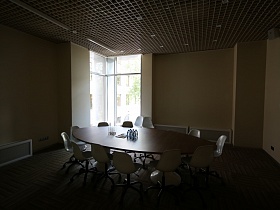 общий вид комнаты для переговоров в деревне с белыми пластиковыми стульями вокруг большого овального стола, мозаичным коричневым подвесным потолком и телевизором на стене
