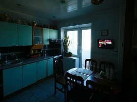 круглые часы и телевизор на белой стене,комнатные цветы на подоконнике с балконной дверью на кухне квартиры оператора