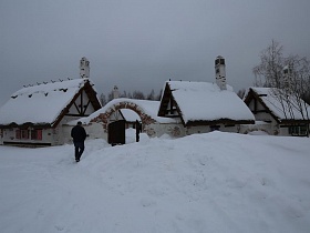 сугробы снега у небольших домиков на территории ресторана, стилизованного под хутор в коттеджном поселке