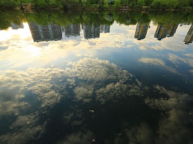 зеркальное отражение белых перистых облаков и синего неба в спокойной воде озера с длинным пирсом