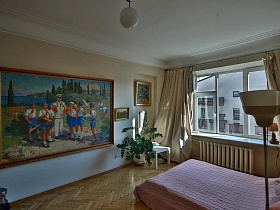 большая кровать, комнатный цветок, белый журнальный столик на паркетном полу спальной комнаты с огромной картиной на стене, посвященной Гагарину в стильной квартире художника