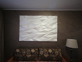 коричневый диван с цветочными подушками, торшер с белым абажуром у темной стены с белым декоративным панно в спальной комнате трехкомнатной квартиры в Измайлово