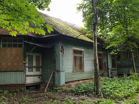 старый заброшенный деревянный одноэтажный дом с окрашенными в голубой цвет стенами, заколоченными дверьми и окнами в лесу
