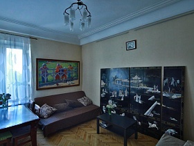 ваза с цветами на черном журнальном столике, большая  модульная картина у стены , белые плафоны люстры на потолке светлой гостиной стильной квартиры художника