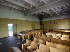 многочисленные светильники на белом потолке с металлическими балками конференц зала с желтыми окрашенными стенами и театральными стульями на сером полу