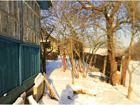 дом с голубой верандой на участке под снегом в окружении деревьев