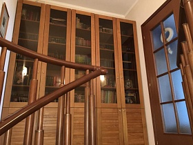 высокий пятидверный деревянный книжный шкаф с книгами на полках у двери со стеклянными вставками в спальную комнату со ступеней винтовой лестницы в светлой студии стильной современной квартиры