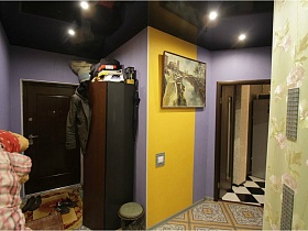 картина на желтой стене, шкаф для одежды у сиреневой стены в прихожей с коричневой входной дверью креативной квартиры с выходом на крышу магазина