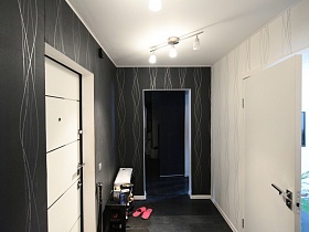 черный столик с полками, обувь на черном полу прихожей с двухцветными обоями-компаньонами на стенах стильной двухкомнатной квартиры