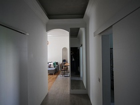 длинный белый коридор с большим прямоугольным зеркалом на стене у арочного дверного проема стильной скандинавской квартиры