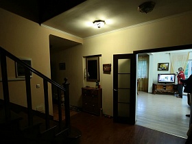 зеркало в рамке над комодом в прихожей с деревянной лестницей и открытыми дверьми в гостиную и кухню семейного дома в глухом лесу