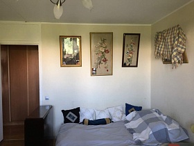 картины в рамке с цветочной композицией над разложенным диваном с многочисленными маленькими подушками на сером покрывале в углу и раскладной стол у открытой входной двери в гостиную квартиры в Бибирево