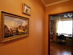 фотография и картина в красивой рамке на светло-коричневой стене у открытой двери в детскую комнату трехкомнатной квартиры государственного служащего