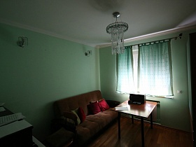 пианино с нотами, стул, коричневый диван с квадратными подушечками, квадратный стол у окна с короткими шторами голубой спальни дизайнерской квартиры