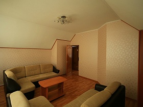 просторная комната отдыха с мягкой мебелью, бежевыми стенами и белым потолком на мансарде пустого съемного дома в сосновом лесу