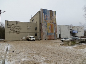 Граффити на высокой, центральной стене и росписи на панелях здания ДК СССР , требующего ремонта с припаркованными машинами на площади у сквера