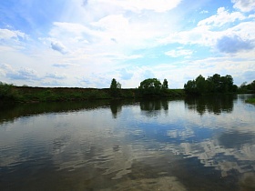 отражение в водной глади реки синего неба и белых облаков, протекающей в живописном месте Подмосковья