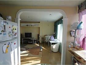белый холодильник и столик у арочного дверного проема из кухни в гостиную евро квартиры с видом на Москву и парк