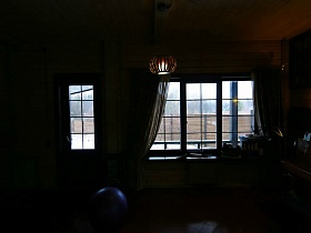 высокий деревянный забор участка загородного дома через стекла большого окна и входной двери