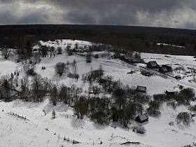 деревья и кустарники на больших участках под снегом с одинокими деревянными домами в заброшенной деревне