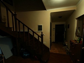 желтые стены прихожей с видеодомофоном у входной двери, зеркалом над комодом и деревянной лестницей в современном семейном доме в глухом лесу
