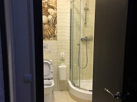 квадратная бежевая плитка на стенах и полу ванной комнаты с санузлом и прозрачной душевой кабиной в современном гостиничном номере
