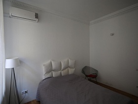 белый кондиционер на стене над белым торшером в светлой спальне с белыми гардинами на окне скандинавской квартиры