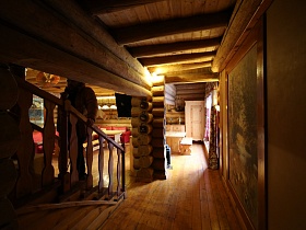 длинный коридор с большой картиной на стене, лестницей с перилами, деревянным полом и балками на потолке дома из сруба