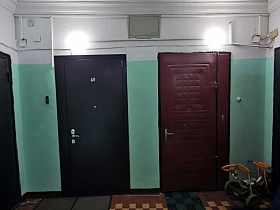светильники с круглыми плафонами на белой стене с бирюзовыми панелями на лестничной площадке с входными дверьми в жилые квартиры сталинского дома времен СССР