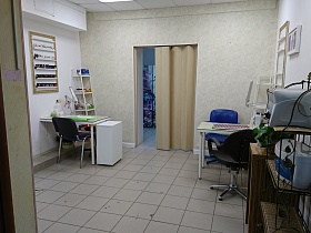 два оборудованных рабочих места на полу с квадратной бежевой плиткой светлой комнаты маникюрного кабинета с бежевой шторой на дверном проеме