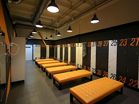 ораньжевые банкетки на полу с серой плиткой в просторной спортивной ораньжевой раздевалке