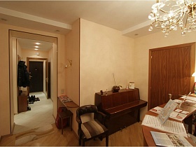 полукруглое кресло с полосатой подушкой у коричневого пианино в комнате с ресепшн съемной трехкомнатной квартиры