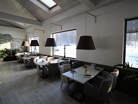 мягкие кресла у сервированных столиков с индивидуальным освещением светильников с большим темным абажуром вдоль стены с окнами