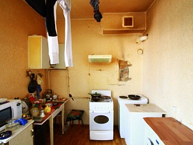 грязная вентиляционная вытяжка под потолком, оборванные старые обои на стенах кухни нищей квартиры в жилом доме
