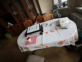 ноутбук на подставке, стопка бумаг на круглом столе с белой в цветочек скатертью в гостиной квартиры сталинки