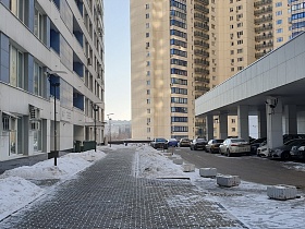 современные высотные жилые дома с тротуарной плиткой на пешеходных дорожках, парковочными местами под навесом с крышей