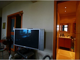 серебристый плоский телевизор, вентилятор, стул у светлой стены между открытыми дверьми в разные комнаты двушки с видом на Москва-сити