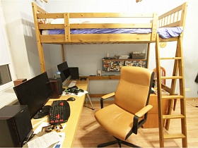компьютерное кресло у длинного письменного стола , шкафчики и кровать в деревянной мебельной стенке детской комнаты современной трехкомнатной квартиры