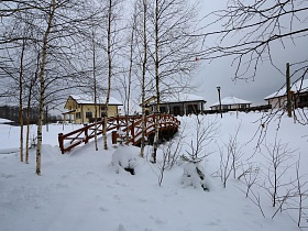 деревянный мостик с перилами среди белых стволов берез под снегом от ресторана к коттеджному поселку