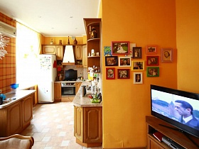 множество фотографий в разноцветных рамочках на ораньжевой стене кухни трехкомнатной  квартиры № 16