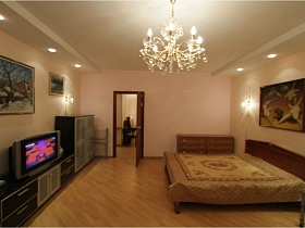картины на светлых стенах гостиной с большой кроватью, комодом и мебельной горкой в съемной трехкомнатной квартире с ресепшн