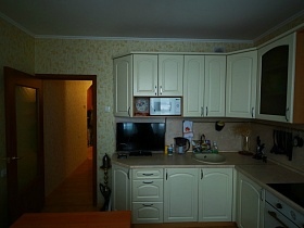 белая микроволновка, плоский телевизор, кувшин и прочие кухонные принадлежности на светлой столешнице белой кухни в большой трехкомнатной квартире после переезда