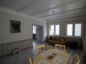 ковер на полу рядом с коричневым мягким диваном с подушечками у окон светлой гостиной с декоративными панелями на бежевых стенах