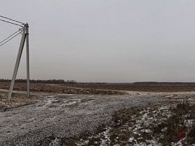 бетонные столбы с проводами электропередач на развилке проселочной дороги у открытого поля в деревне зимой
