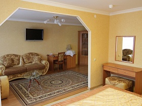 стеклянный овальный журнальный столик на цветном коричневом ковре комнаты отдыха гостиничного номера