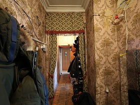 верхняя одежда на крючках настенной вешалки, трюмо, шторы с бахрамой в коридоре с цветными простыми обоями советского времени