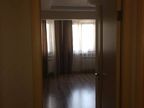коричневые шторы и белая гардина на большом окне гостиной с полосатым линолеумом на полу современной семейной квартиры с дизайнерским ремонтом